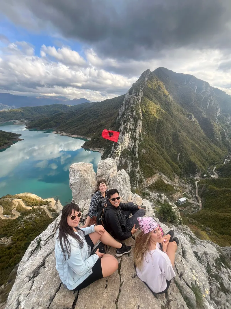 Four people sitting on a rocky mountain peak overlooking a lake.