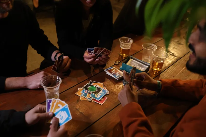 A group of people playing a card game around a wooden table.